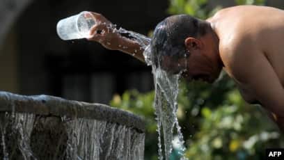 Seorang pria mendinginkan dirinya dengan air dari air mancur (SinPo.id/ AFP)