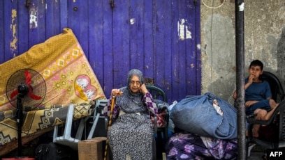 Seorang perempuan dan anak menunggu dengan barang-barangnya sebelum dievakuasi dari Rafah di Jalur Gaza selatan (SinPo.id/AFP)