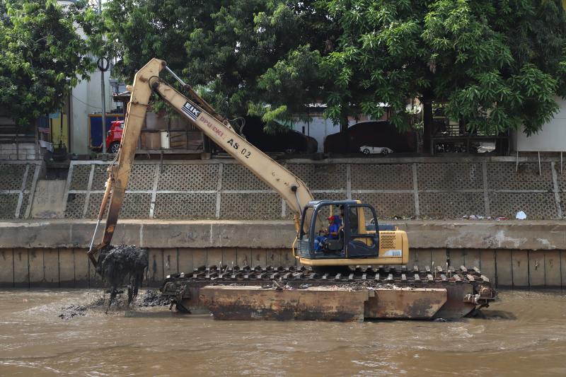 Petugas Dinas Sumber Daya Air Jakarta sedang melakukan pengerukan lumpur menggunakan alat berat ekskavator untuk mencegah terjadinya banjir ketika musim hujan datang (Ashar/SinPo.id)