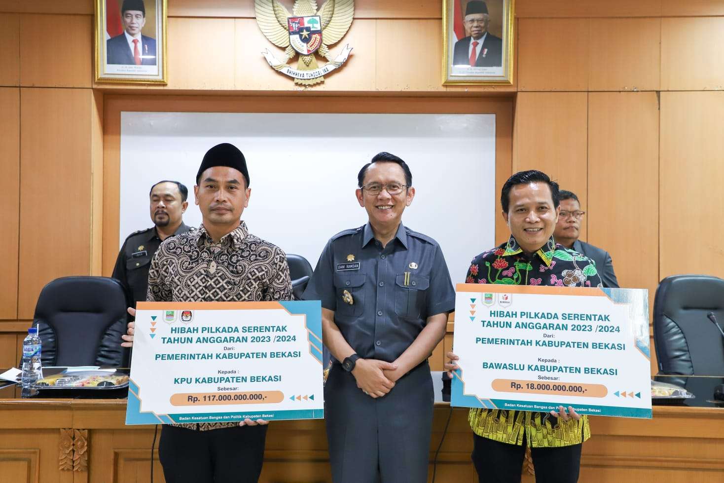 Pj Bupati Bekasi Dani Ramdan secara simbolis menyerahkan dana hibah kepada Ketua KPU Kabupaten Bekasi, Jajang Wahyudin dan Ketua Bawaslu Kabupaten Bekasi, Akbar Khadafi (SinPo.id/Pemkab Bekasi)