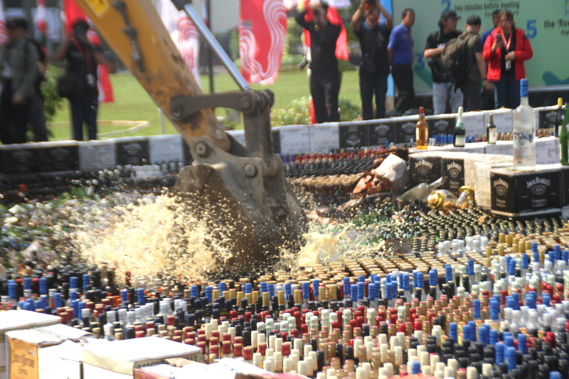 Petugas Bea Cukai sedang memusnahkan ratusan ribu botol minuman keras dan rokok ilegal yang merugikan negara sebesar Rp 165 miliar (Ashar/SinPo.id)