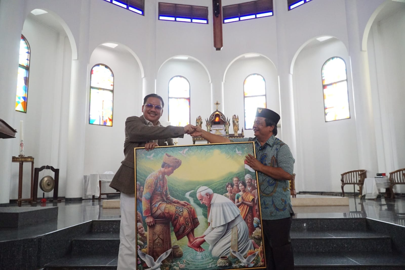 Ketua Esoterika Forum Spiritualitas, Denny JA menyerahkan lukisan kepada Pastor Kepala Paroki Gereja Katolik Santo Servatius Romo Yohanes Wartaya SJ di Kampung Sawah Bekasi (Ashar/SinPo.id)