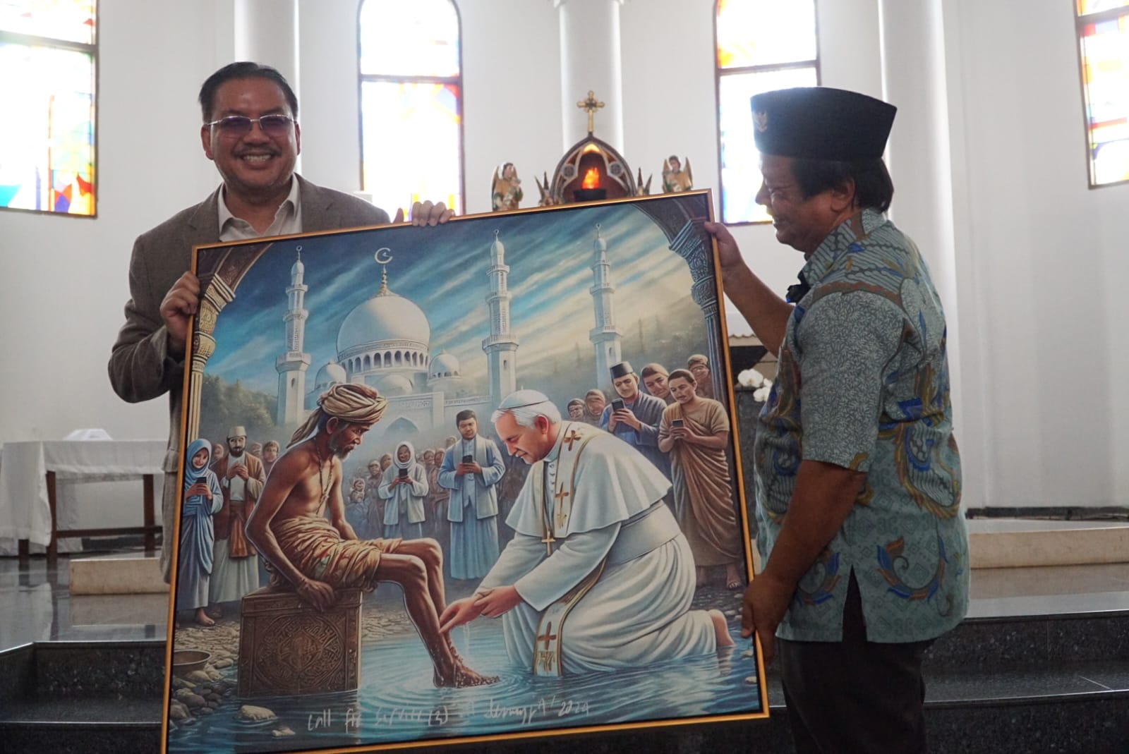 Ketua Esoterika Forum Spiritualitas, Denny JA menyerahkan lukisan kepada Pastor Kepala Paroki Gereja Katolik Santo Servatius Romo Yohanes Wartaya SJ di Kampung Sawah Bekasi (Ashar/SinPo.id)