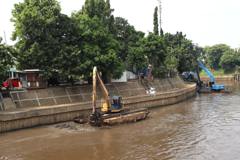 Petugas Dinas Sumber Daya Air Jakarta sedang melakukan pengerukan lumpur menggunakan alat berat ekskavator untuk mencegah terjadinya banjir ketika musim hujan datang (Ashar/SinPo.id)