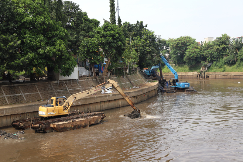 Petugas Dinas Sumber Daya Air Jakarta sedang melakukan pengerukan lumpur menggunakan alat berat ekskavator untuk mencegah terjadinya banjir ketika musim hujan datang (Ashar/SinPo.id)