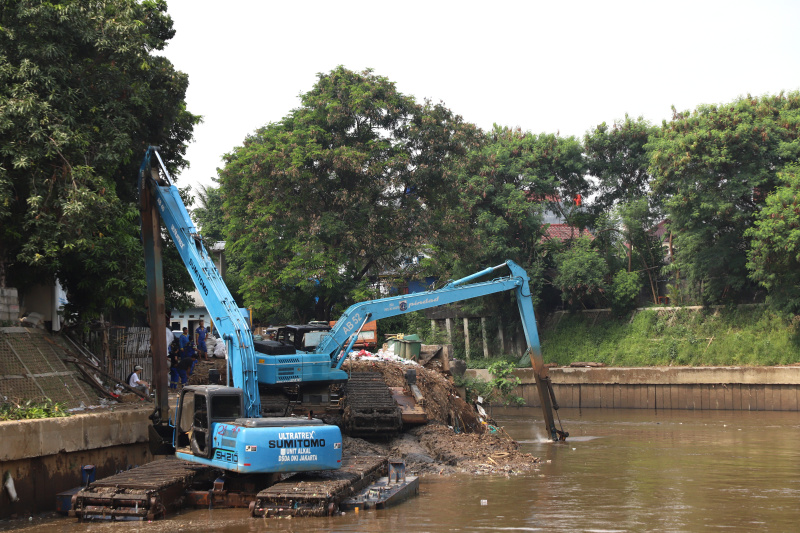 Petugas Dinas Sumber Daya Air Jakarta sedang melakukan pengerukan lumpur menggunakan alat berat ekskavator untuk mencegah terjadinya banjir ketika musim hujan datang (Ashar/SinPo.id)