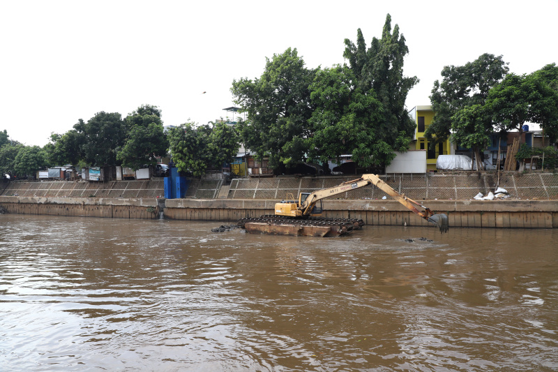 Petugas Dinas Sumber Daya Air Jakarta sedang melakukan pengerukan lumpur menggunakan alat berat ekskavator untuk mencegah terjadinya banjir ketika musim hujan datang (Ashar/SinPo.id)