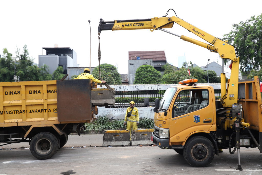 Petugas PPSU dan Dinas Bina Marga Provinsi DKI Jakarta sedang membersihkan jalan dan coretan vandalisme di tembok gedung DPR (Ashar/SinPo.id)