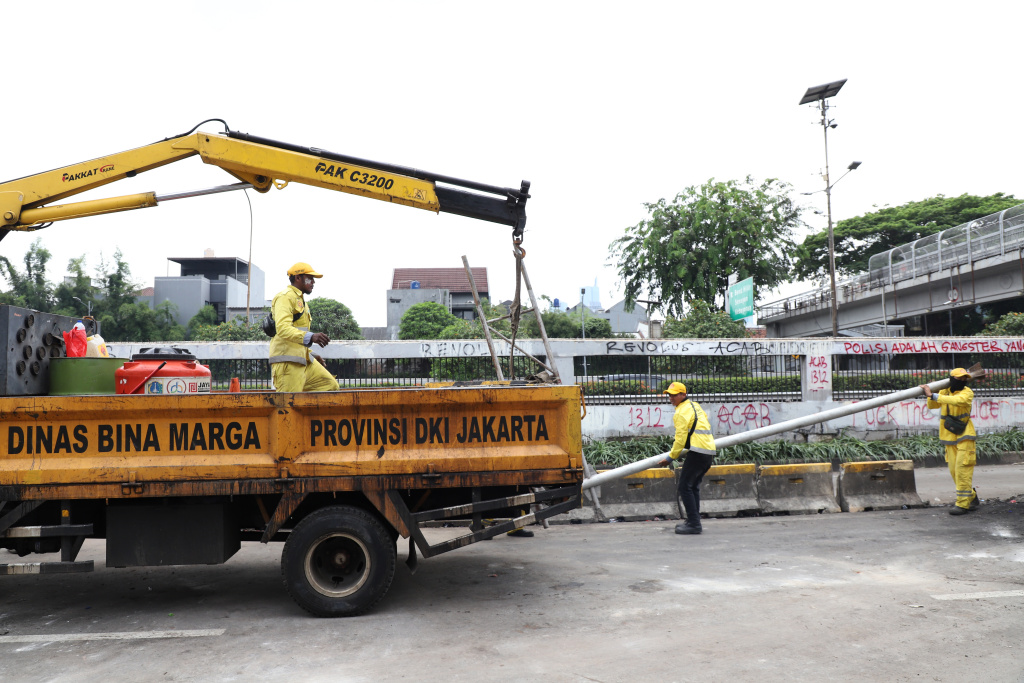 Petugas PPSU dan Dinas Bina Marga Provinsi DKI Jakarta sedang membersihkan jalan dan coretan vandalisme di tembok gedung DPR (Ashar/SinPo.id)
